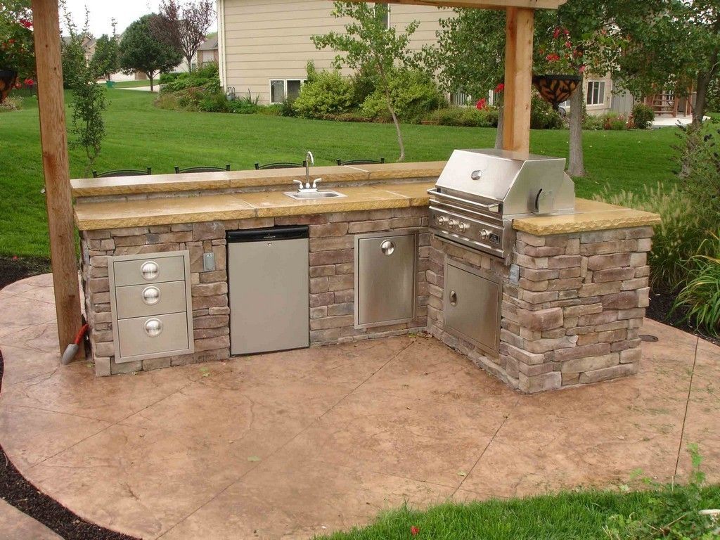 Outdoor stone-and-stainless grilling island with sink and cabinets in a backyard pavilion
