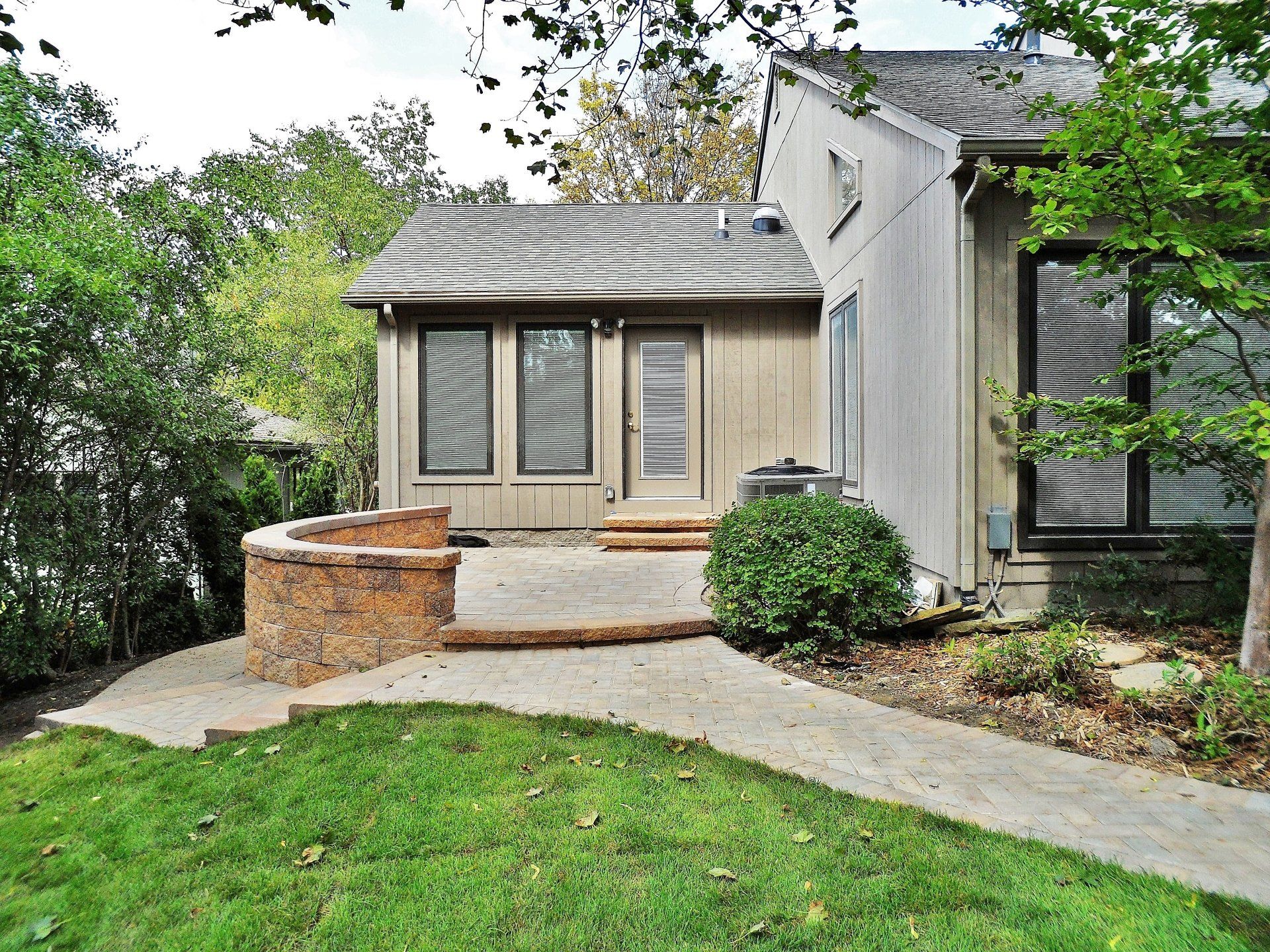 Suburban house entrance with a curved walkway, stone planter, and green lawn.