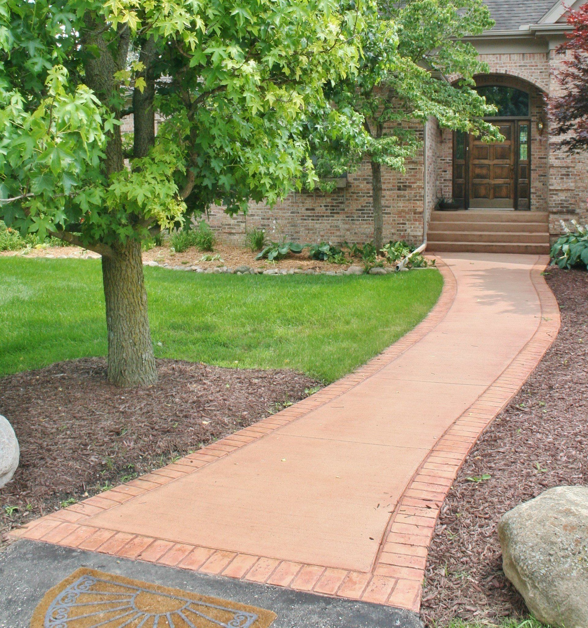 Curved brick walkway leading to a house entrance through a landscaped front yard