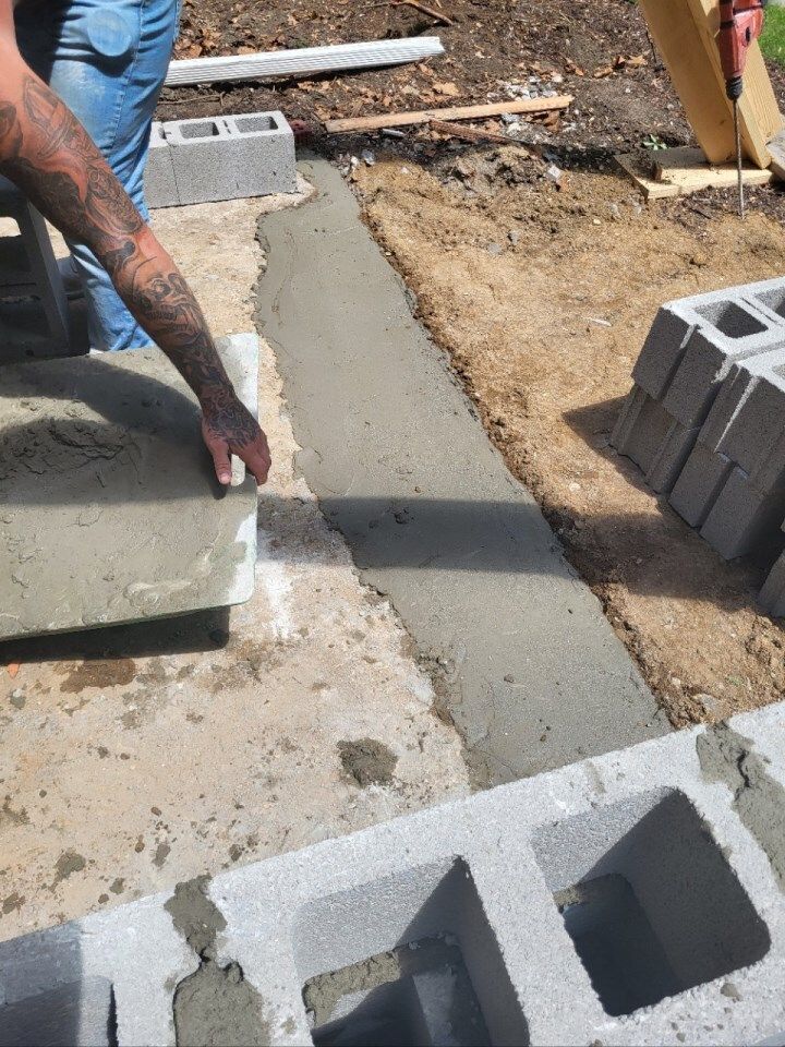 Person spreading wet concrete between cinder blocks at a construction site