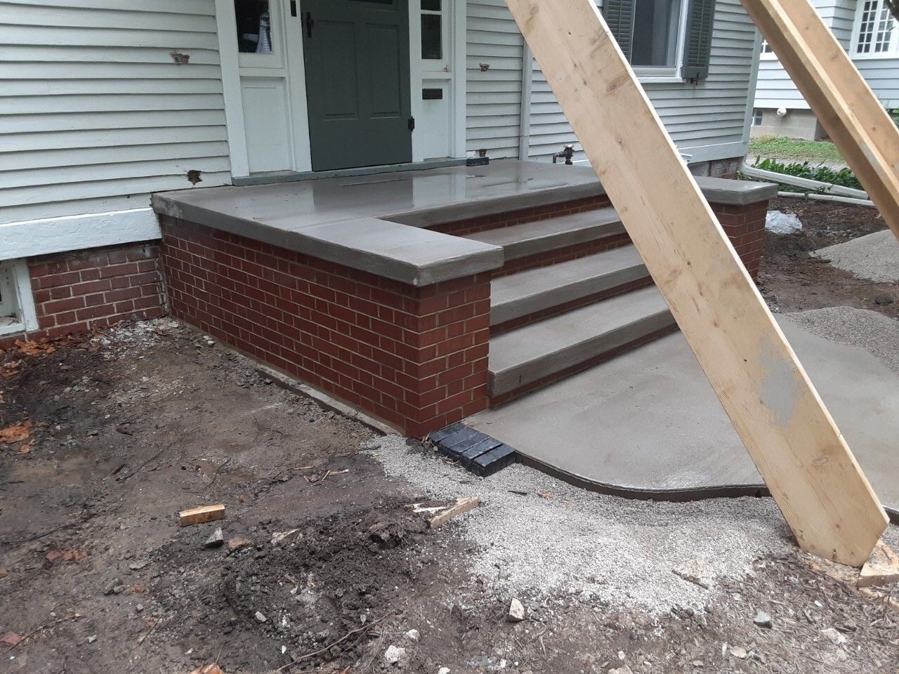 Front porch with brick steps, a leaning wooden beam, and unfinished gravel ground near a house entrance