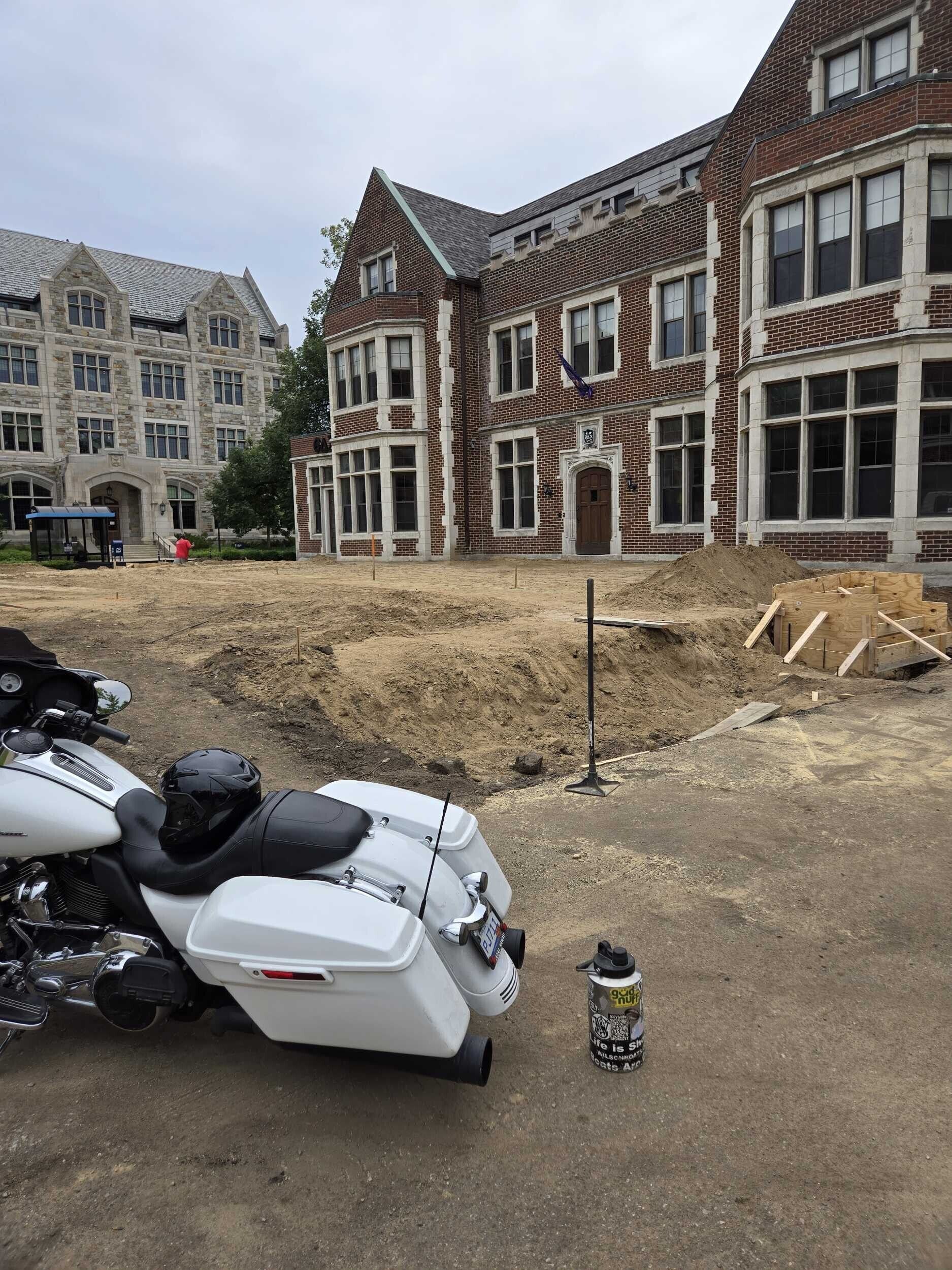 Motorcycles parked beside a dirt lot in front of brick buildings and a partially demolished site
