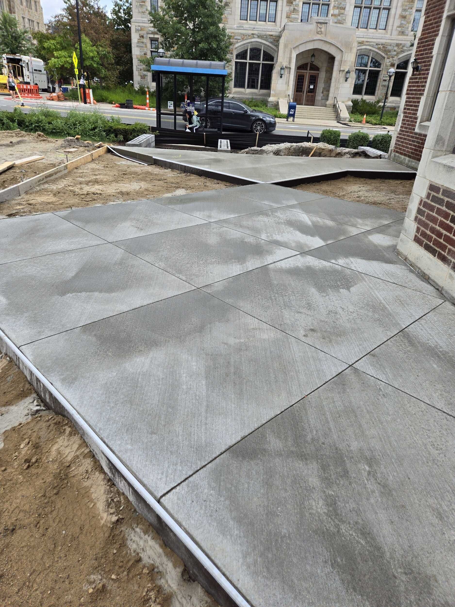 New concrete sidewalk ramp under construction beside a building and parked truck