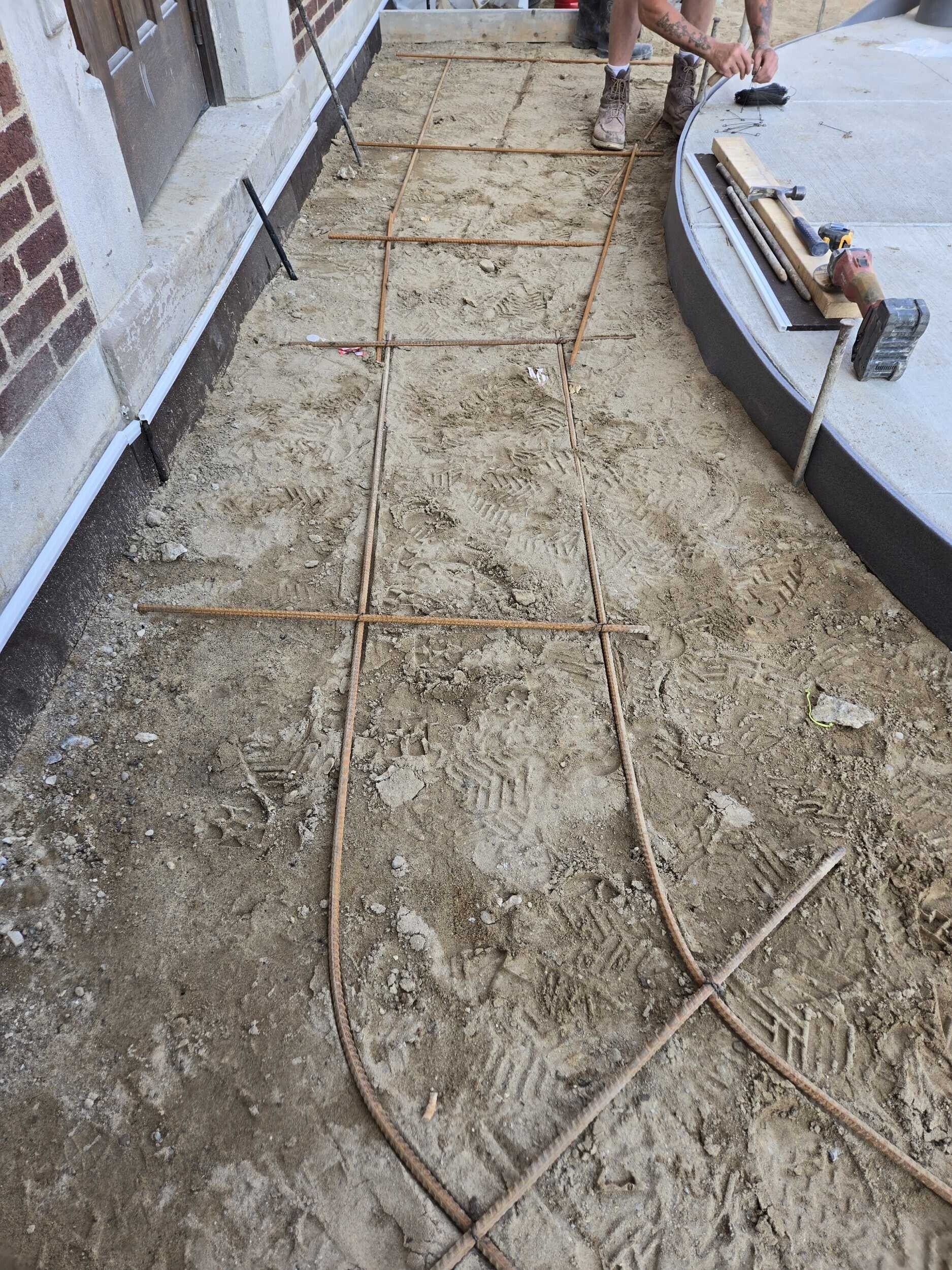 Construction walkway with wet concrete and rebar beside a brick wall and raised curb