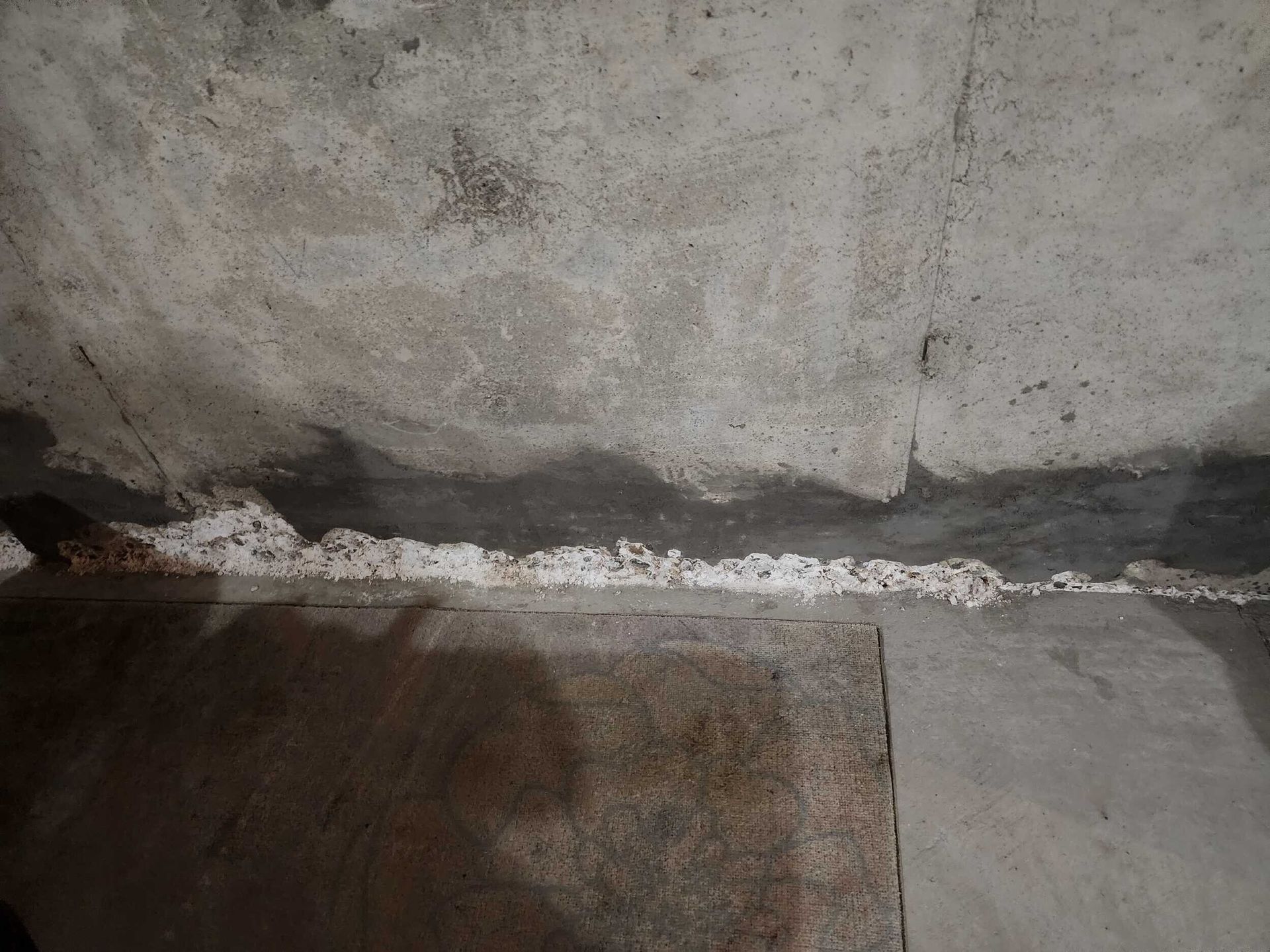 Cracked concrete wall with a dark floor and a white line of debris along the base