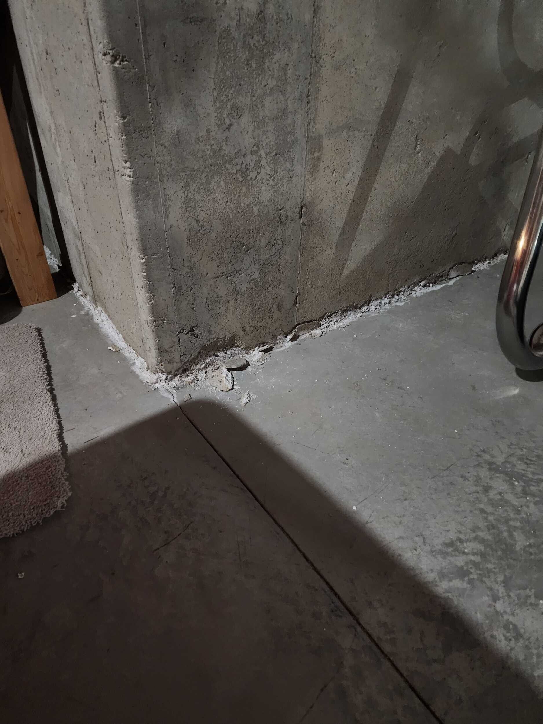 Concrete wall corner with chipped white caulk at the floor and a shadow across the slab.