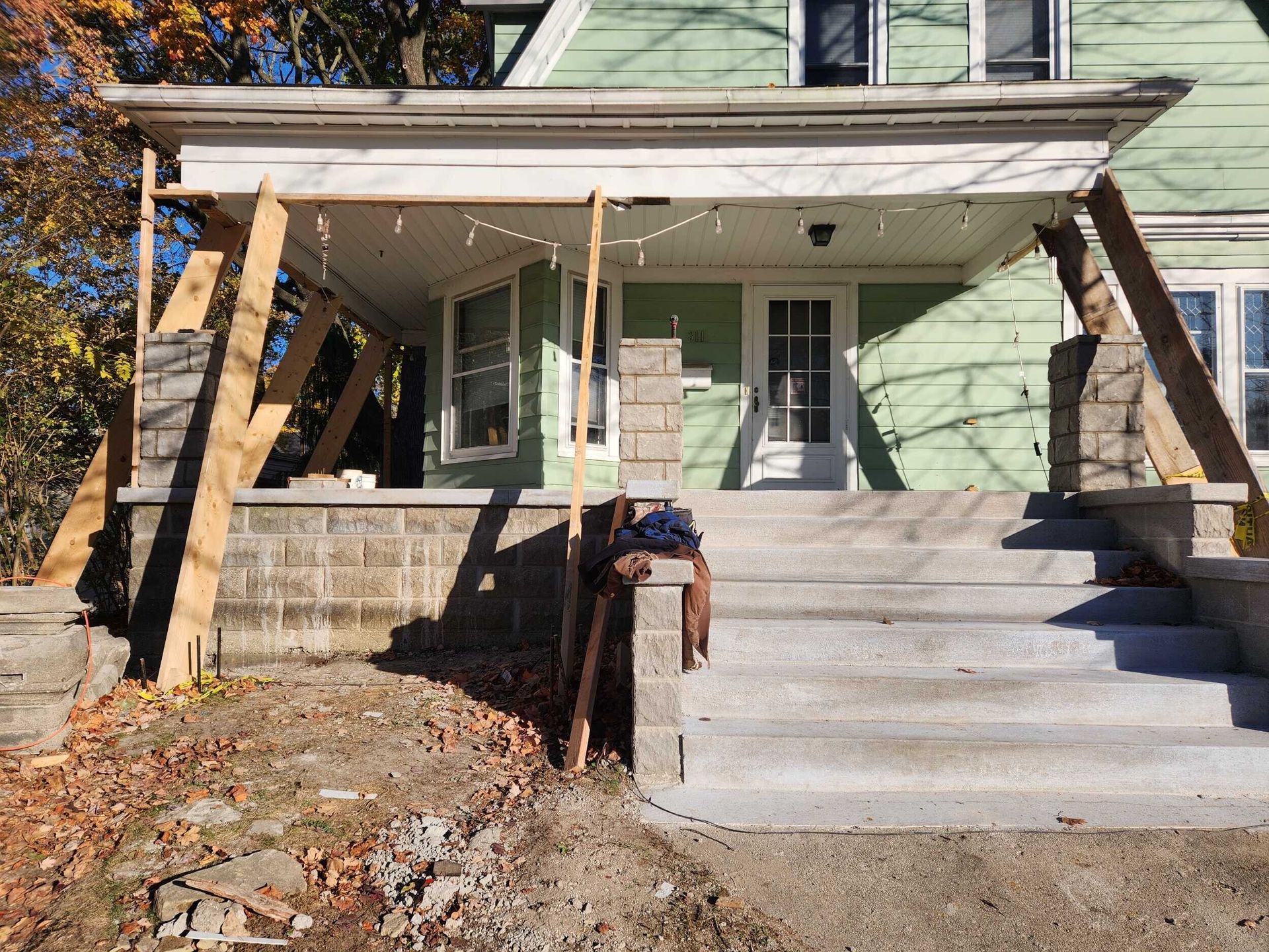 Front porch of a pale green house with stone steps, white columns, and a wooden wheelchair ramp.