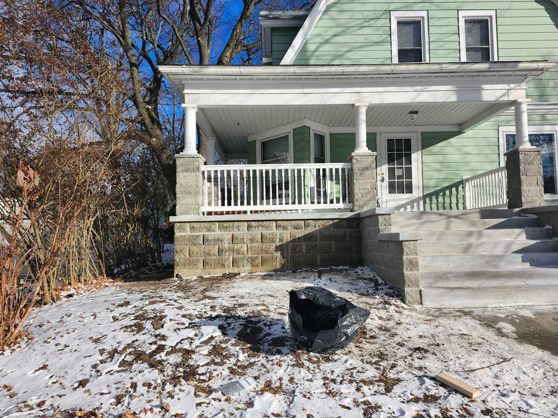 Snow-dusted house with a front porch, stone steps, and a car covered in snow in the yard.