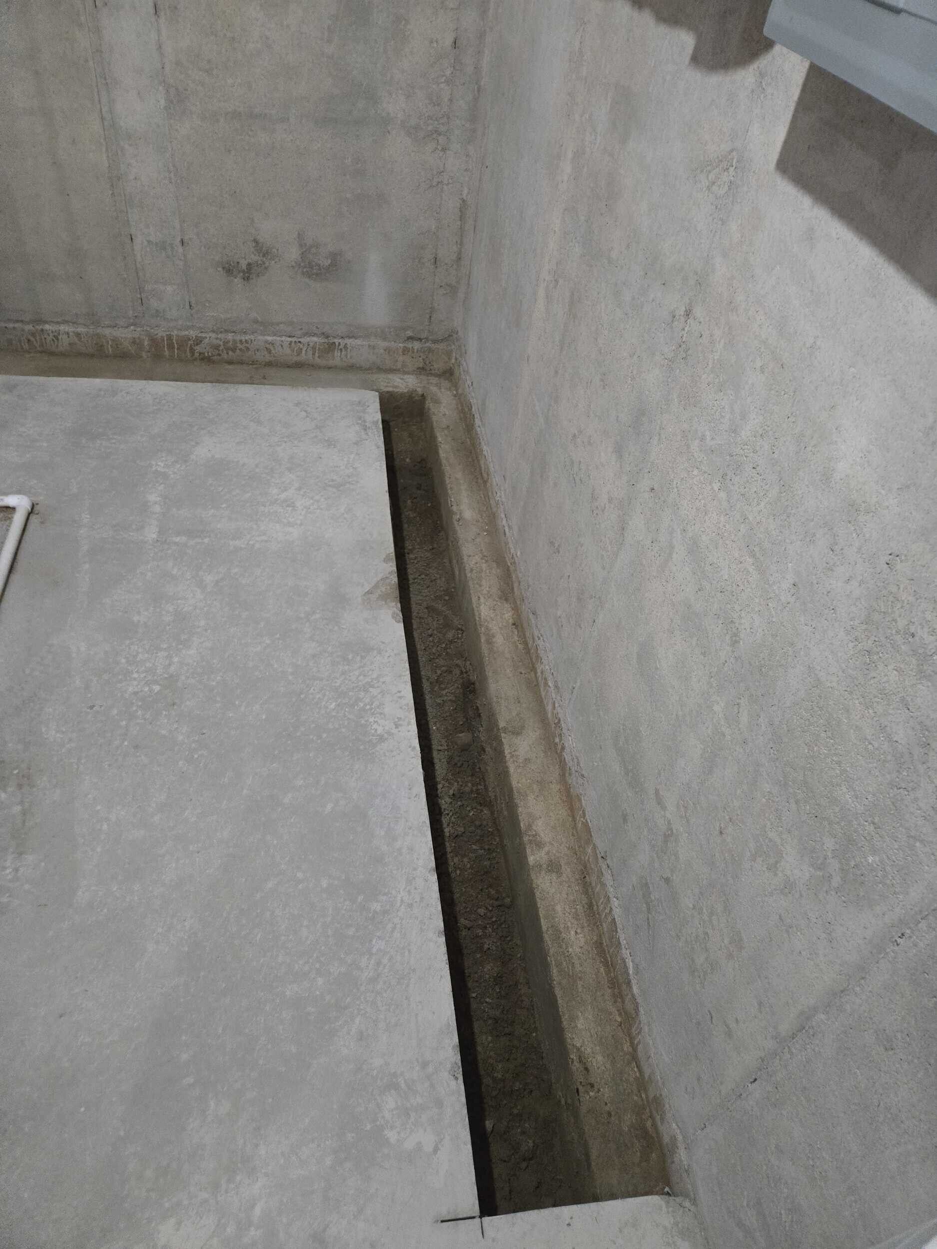Concrete floor beside a narrow open trench along a gray wall