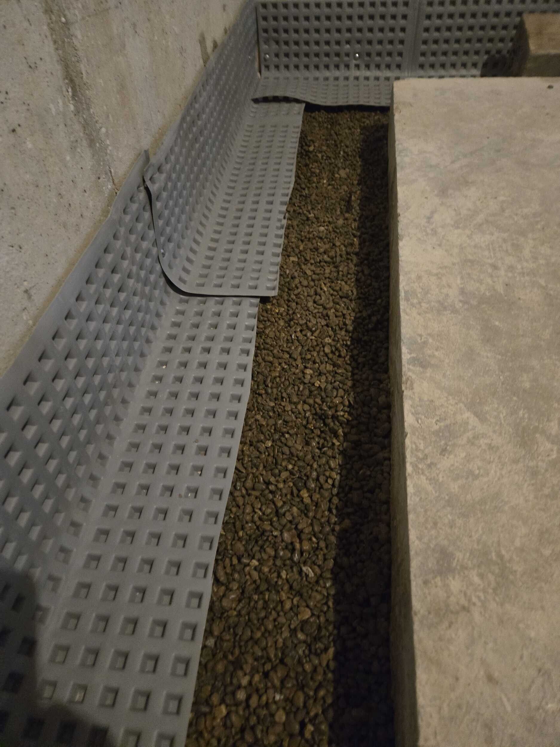 Perforated metal walkway with gravel drain channel beside a concrete wall
