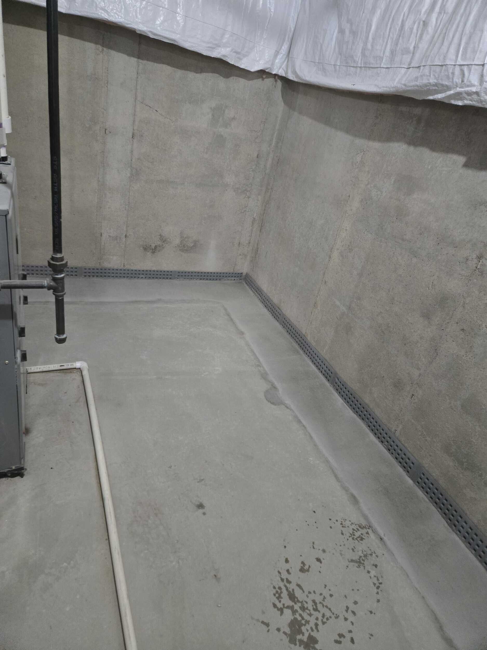 Empty concrete utility area with a gray wall, floor drain, and hanging white tarp overhead