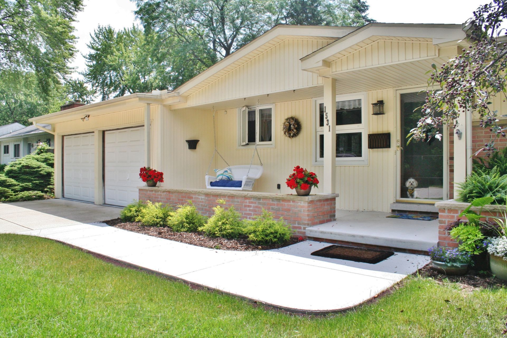 Cream house with garage, front porch, and flower pots beside a curving white walkway