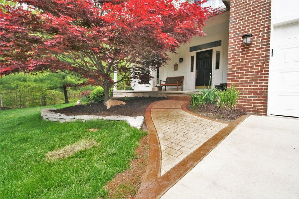 Front yard with a curved concrete walkway beside a brick house and a red-leafed tree