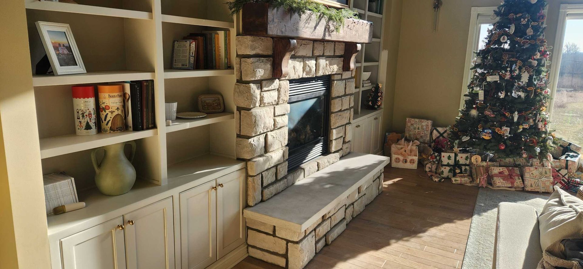 Cozy living room with a decorated Christmas tree, fireplace, built-in shelves, and wrapped gifts.