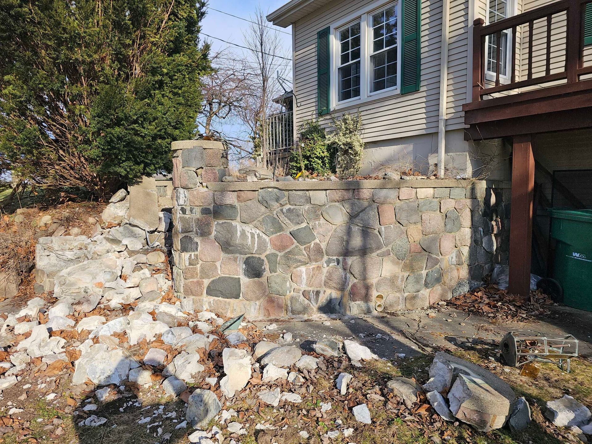 Stone retaining wall under construction beside a house, with rubble and debris in the yard.