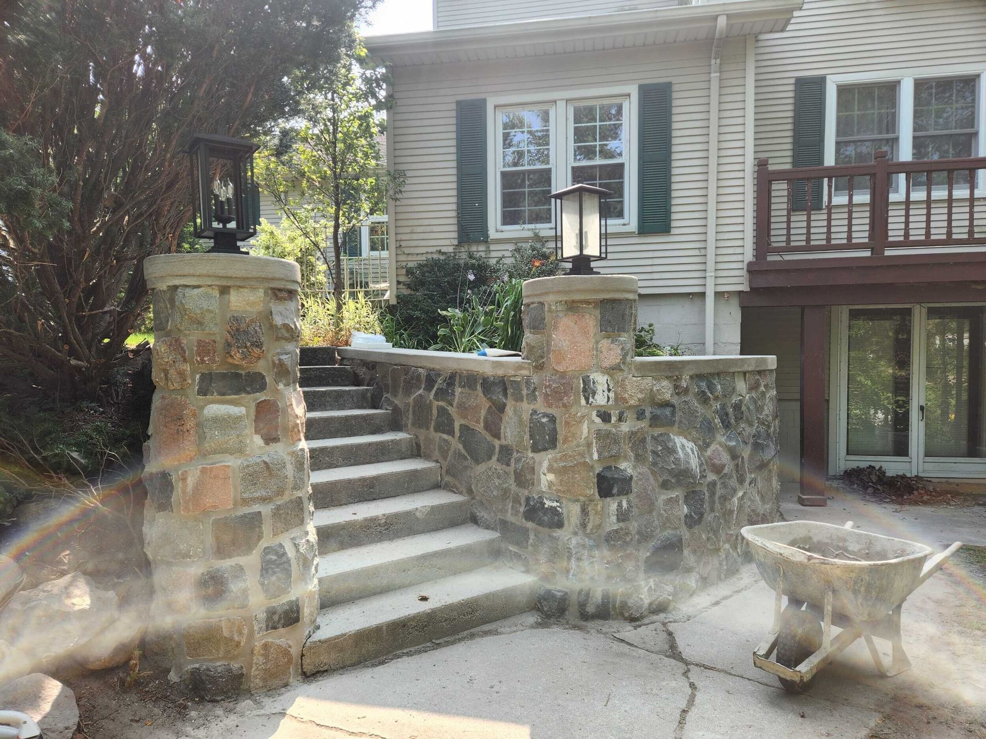 Stone staircase with decorative pillars leading to a house entrance and wooden deck.