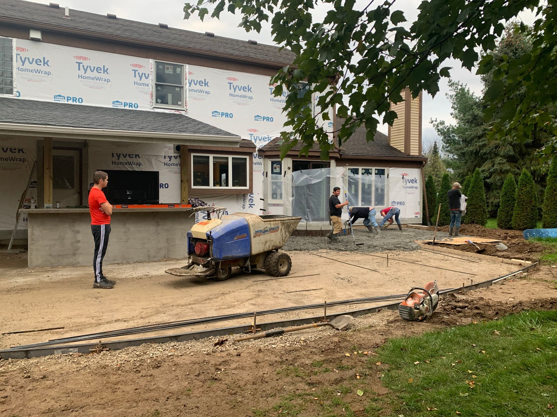 Construction site with workers, a small machine, and a partially finished house exterior