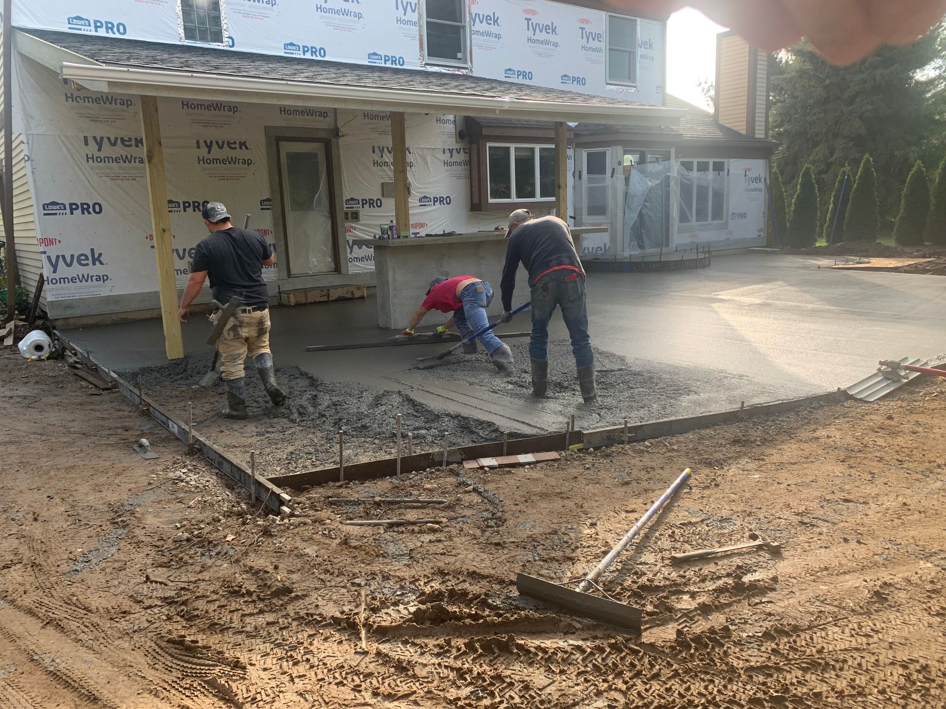 Workers spread wet concrete outside a storefront, leveling a sidewalk in front of shops.