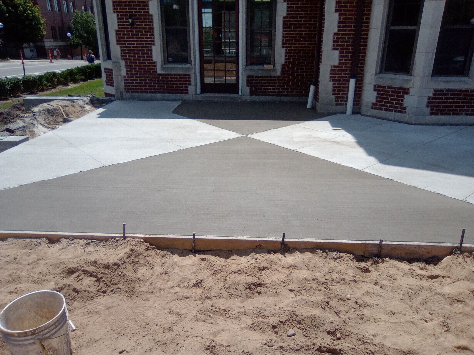 Concrete walkway leading to a brick building entrance, bordered by dirt and fresh construction work