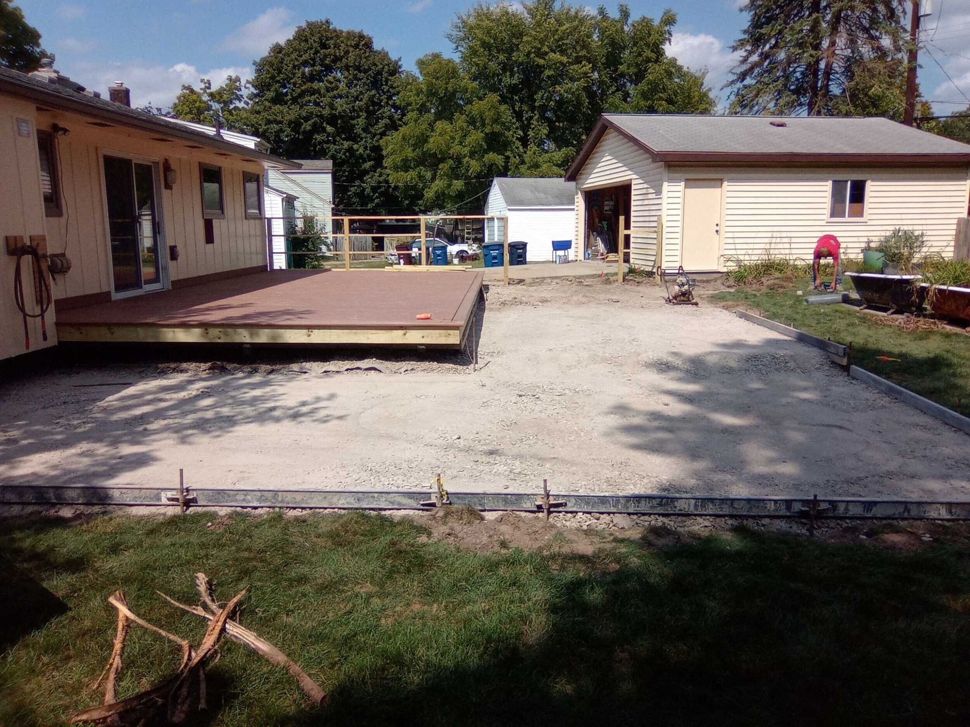 Backyard with a wooden deck, gravel patio, and two sheds beside a house.