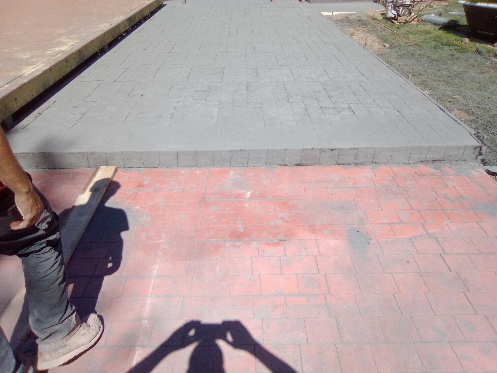 Brick walkway leading to a concrete path, with a person’s leg visible at left and a shadow in the foreground