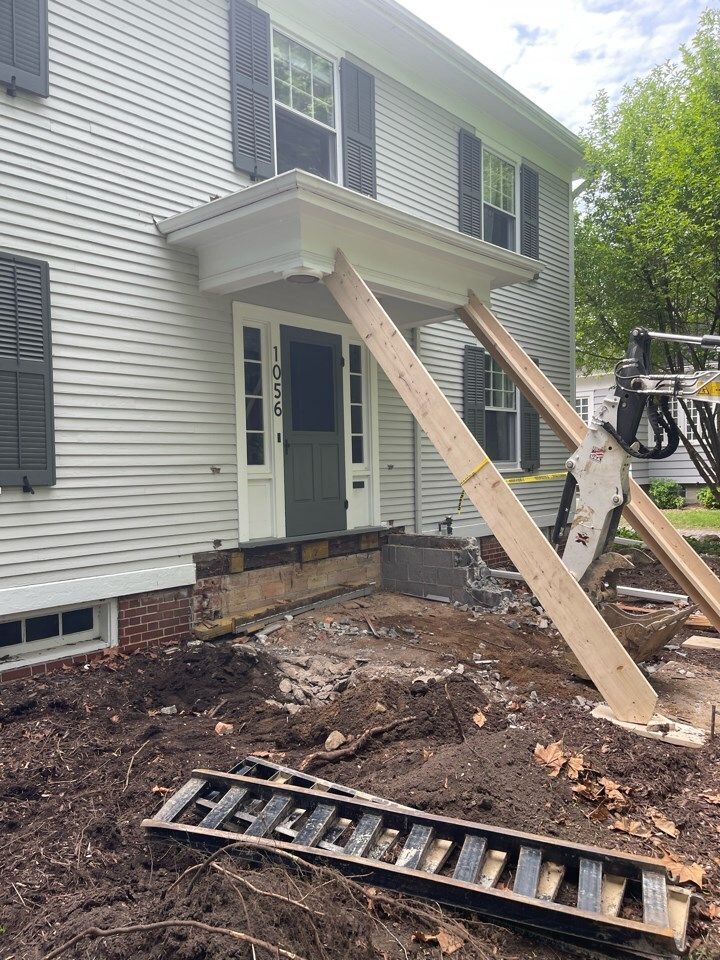 House exterior under renovation with temporary wooden supports, debris, and a ladder in the yard