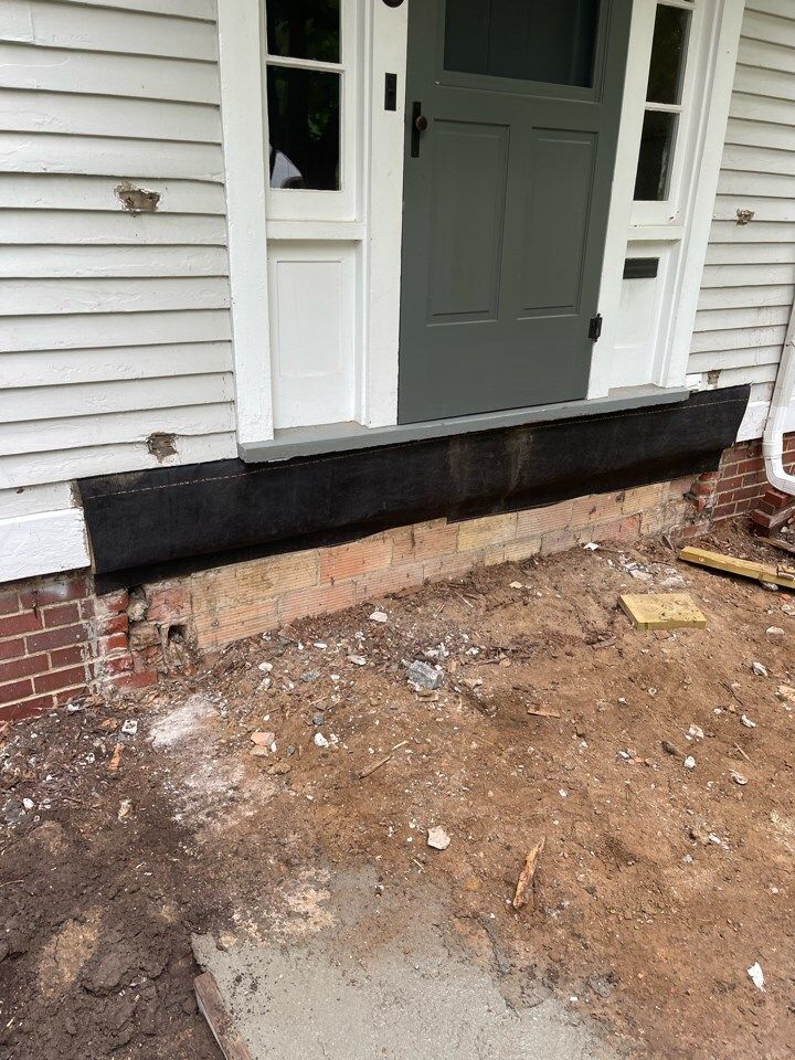 House entry with a damaged front step, exposed brick, and dirt ground in front of the door.