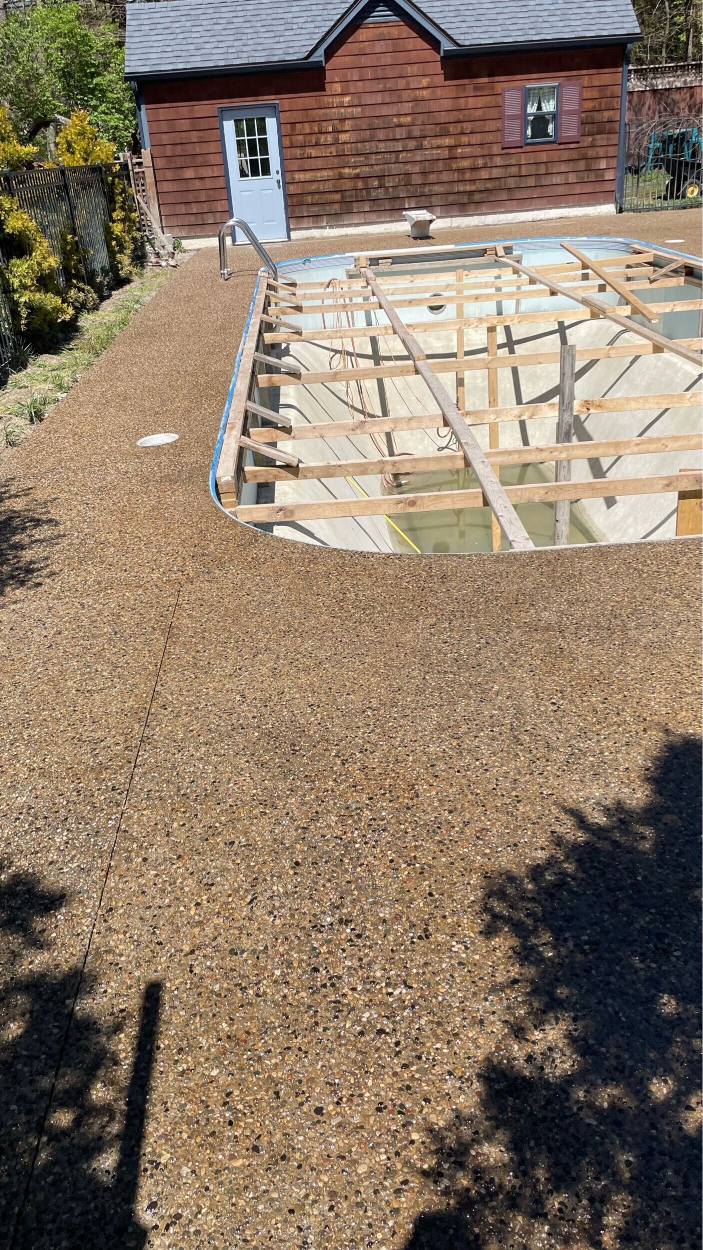 Backyard under construction with exposed wooden deck framing beside a gravel path and brick house