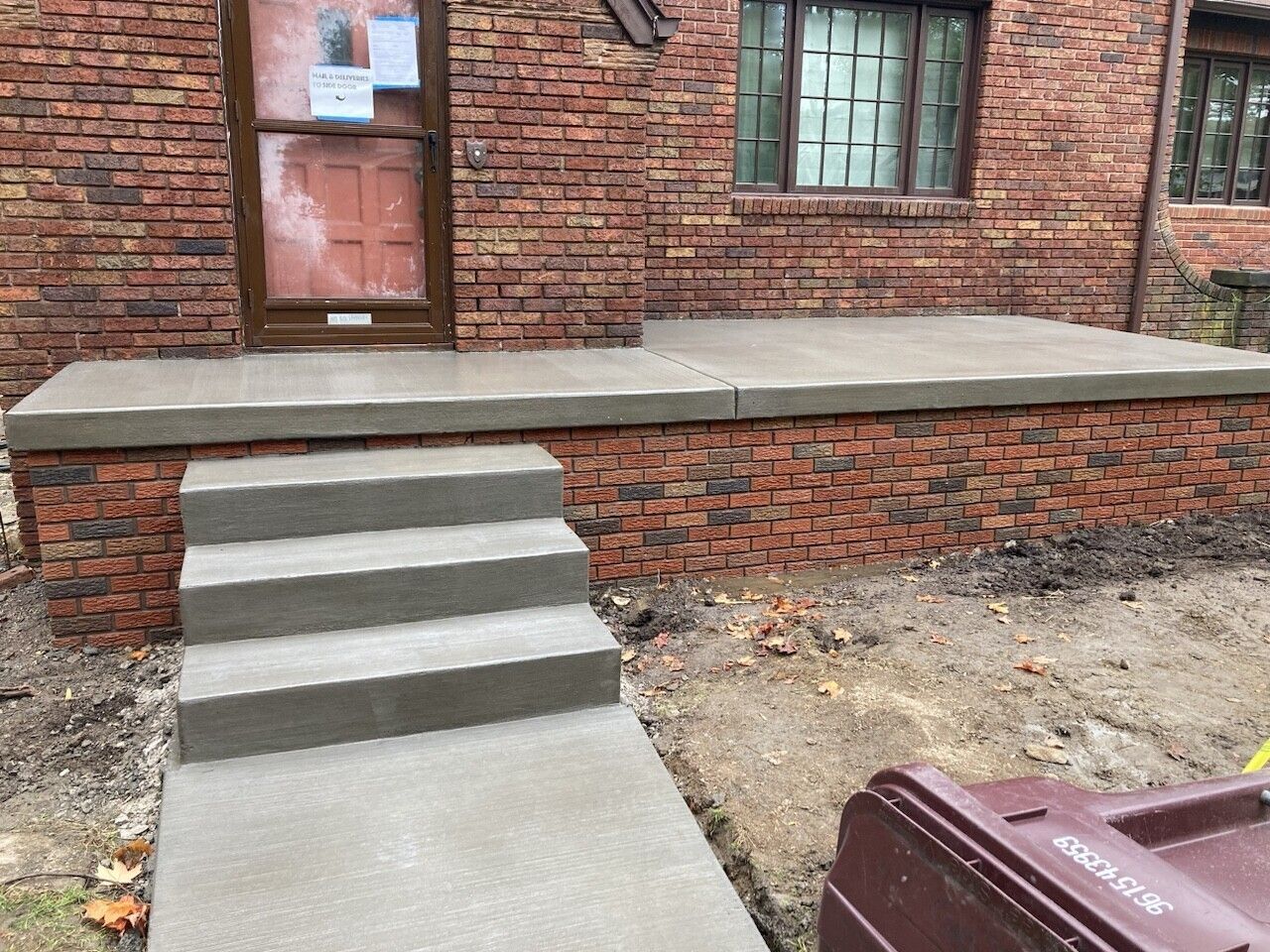 Concrete steps leading to a raised brick porch on a brick building, with a walkway and dirt yard.