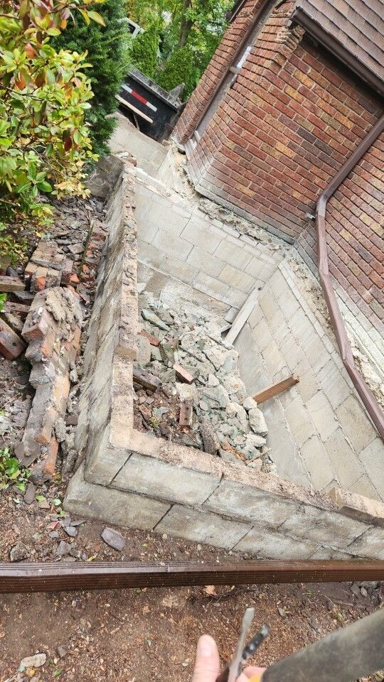Collapsed stone stairway beside a brick wall, with rubble and a car in the background.