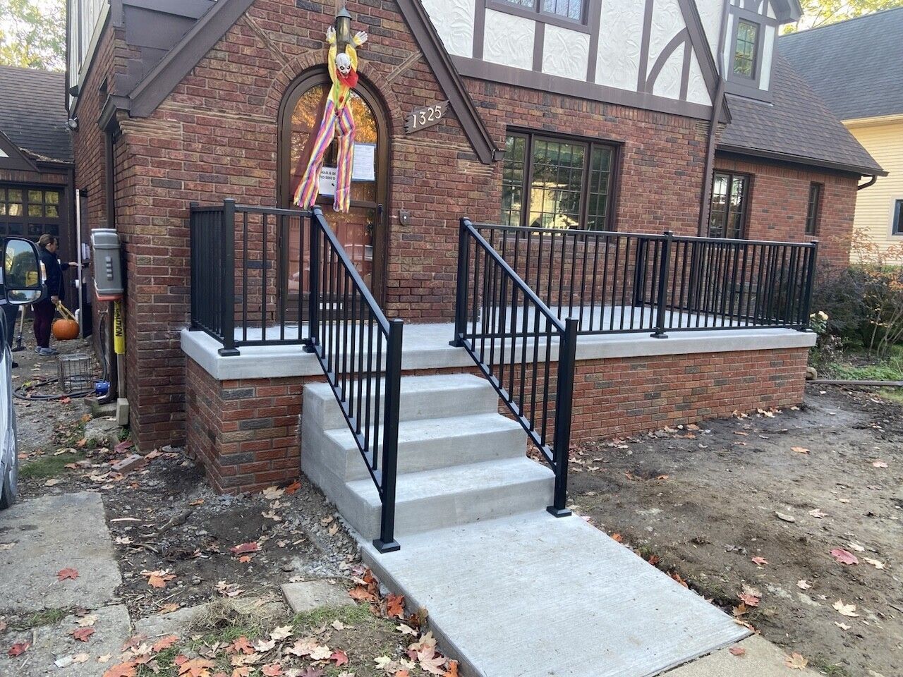 Brick house entrance with concrete steps, black railings, and a decorated porch area