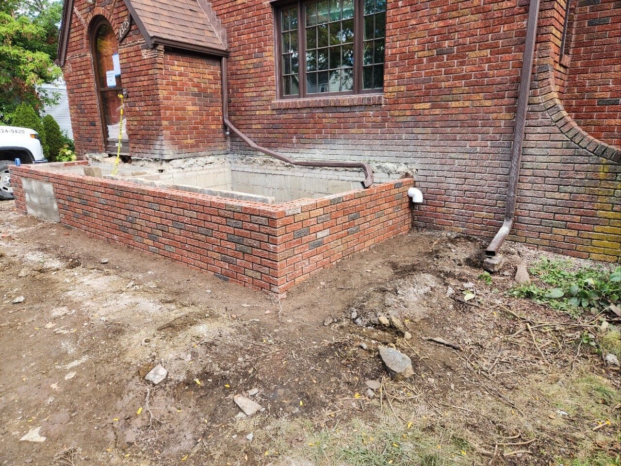 Brick house exterior with a low brick retaining wall and rough dirt yard construction area