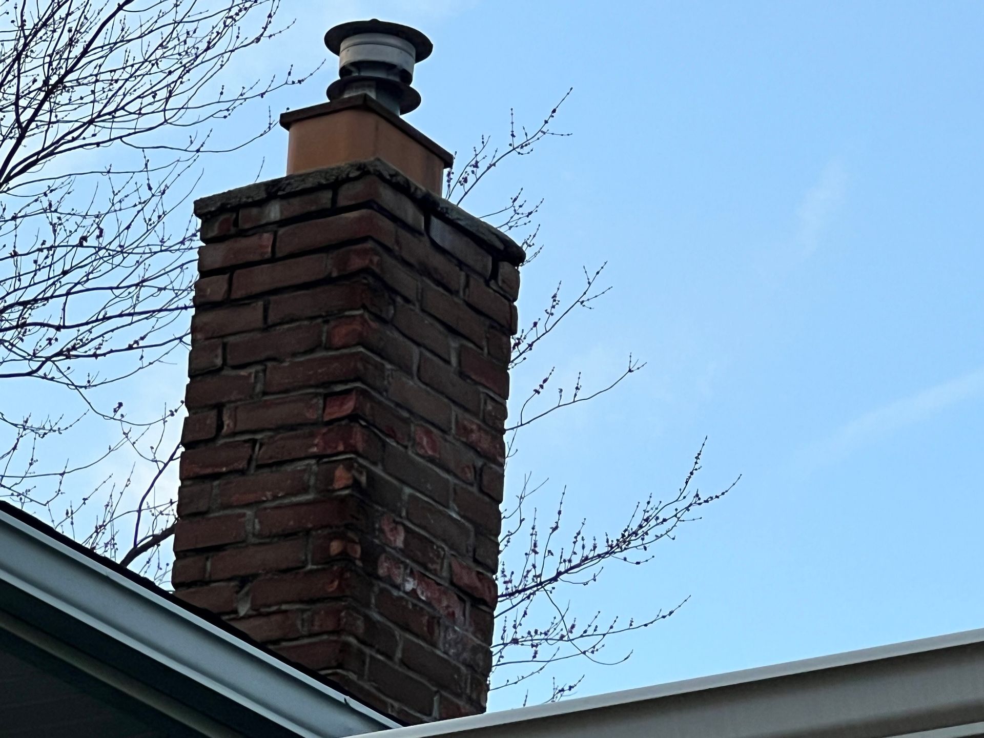 Brick chimney with a metal cap on a rooftop against a blue sky