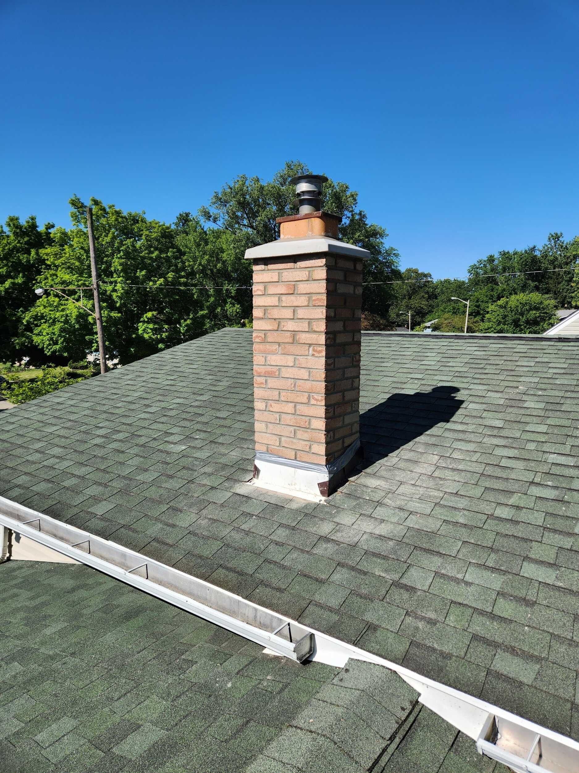 Brick chimney on a green shingled roof under a clear blue sky