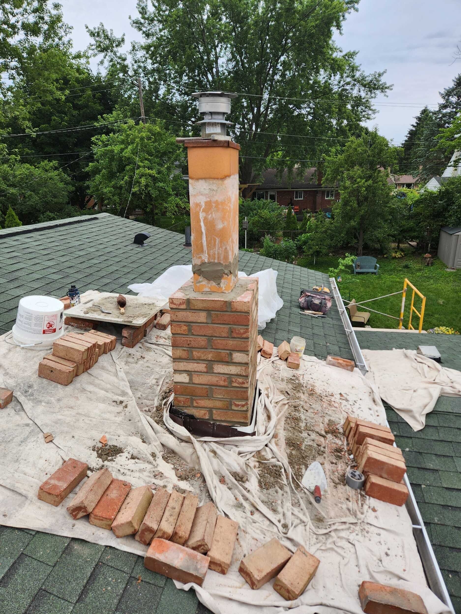 Partially built brick chimney on a rooftop, with construction debris and trees in the background