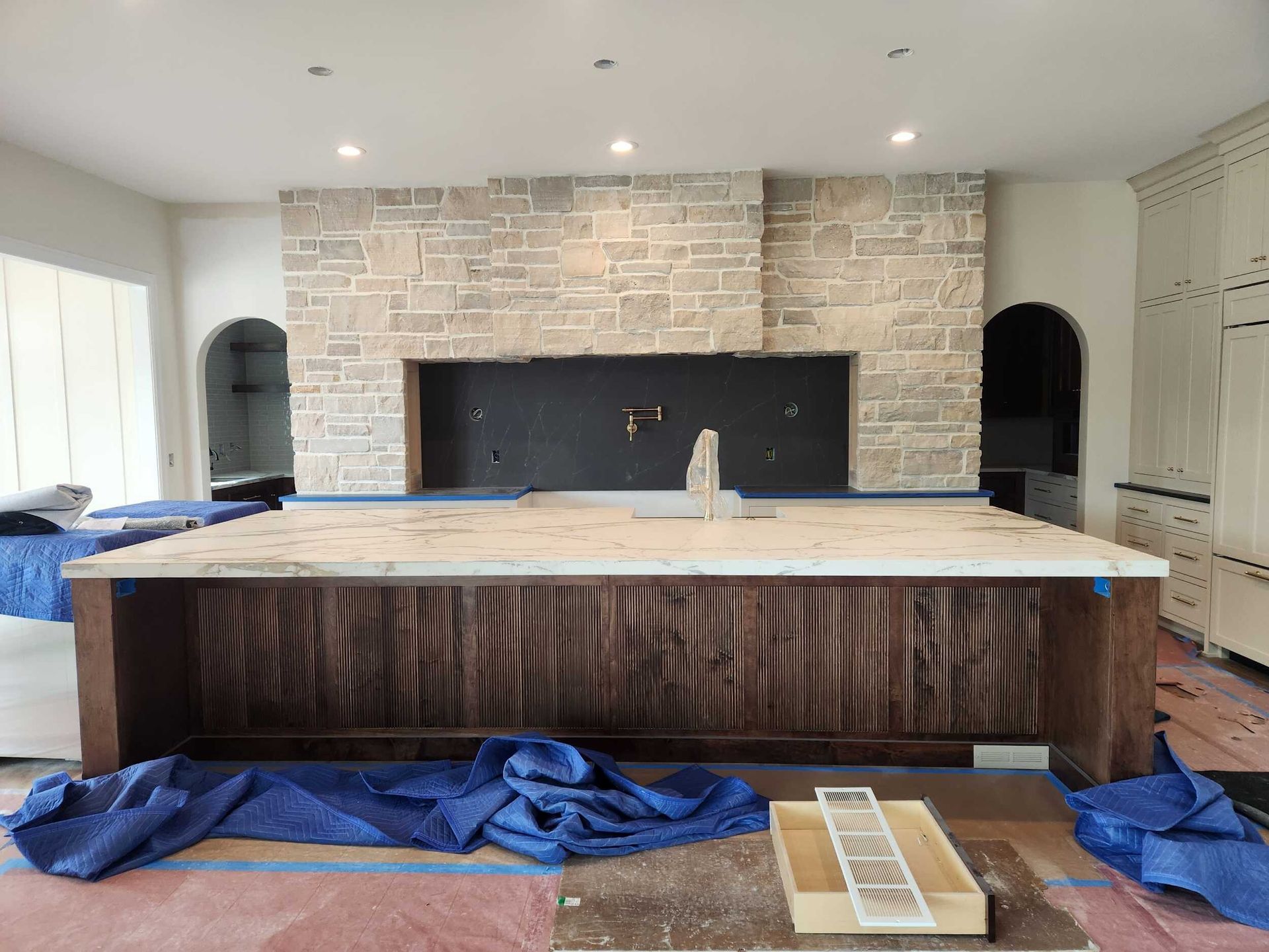 Kitchen under construction with a large wood island, brick backsplash, and blue drop cloths on the floor