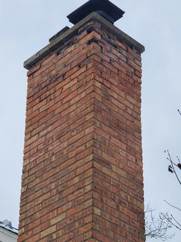 Tall red brick chimney with a dark cap against a cloudy sky