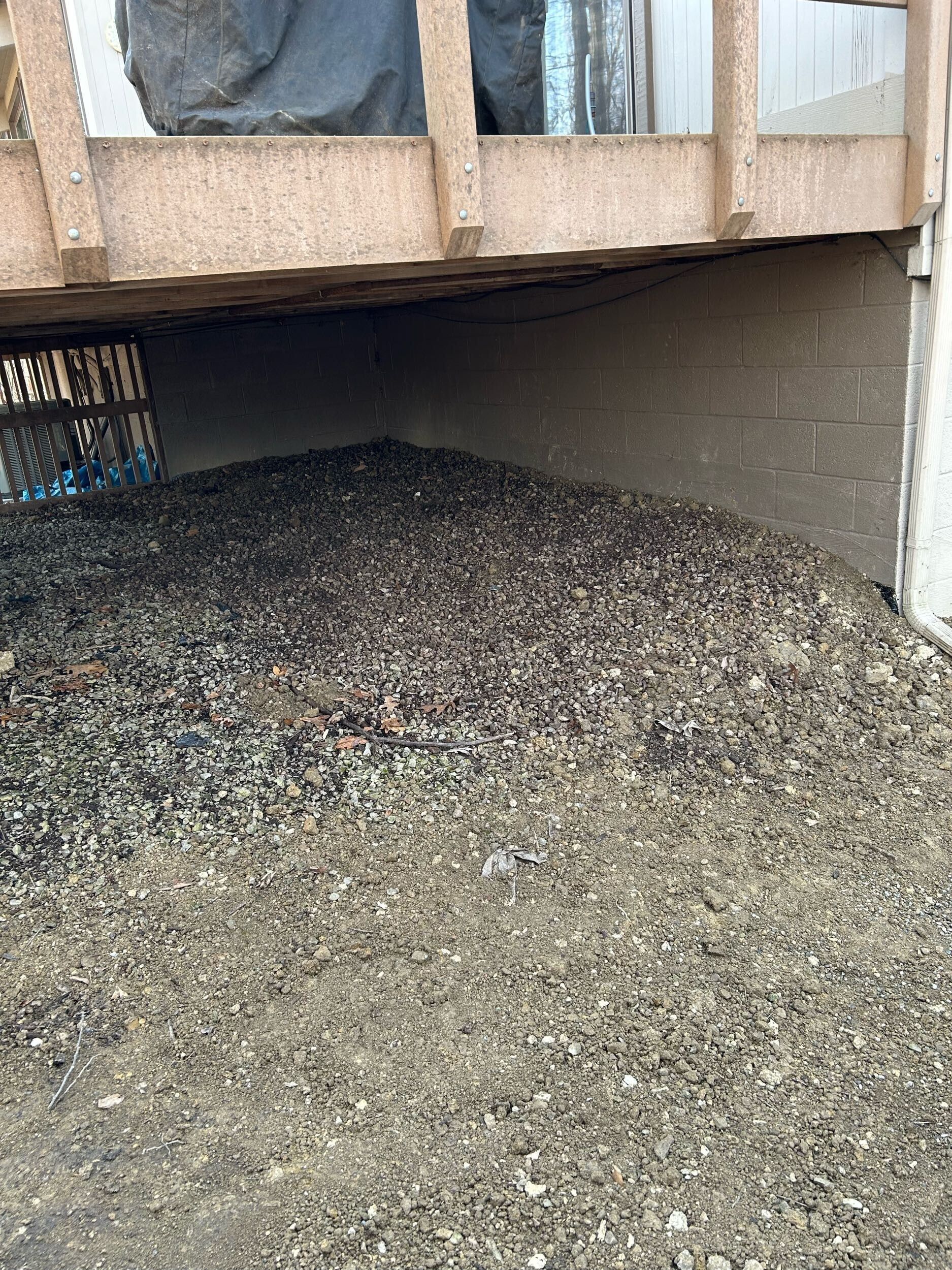 Gravel piled under a raised wooden structure next to a cinder block wall.