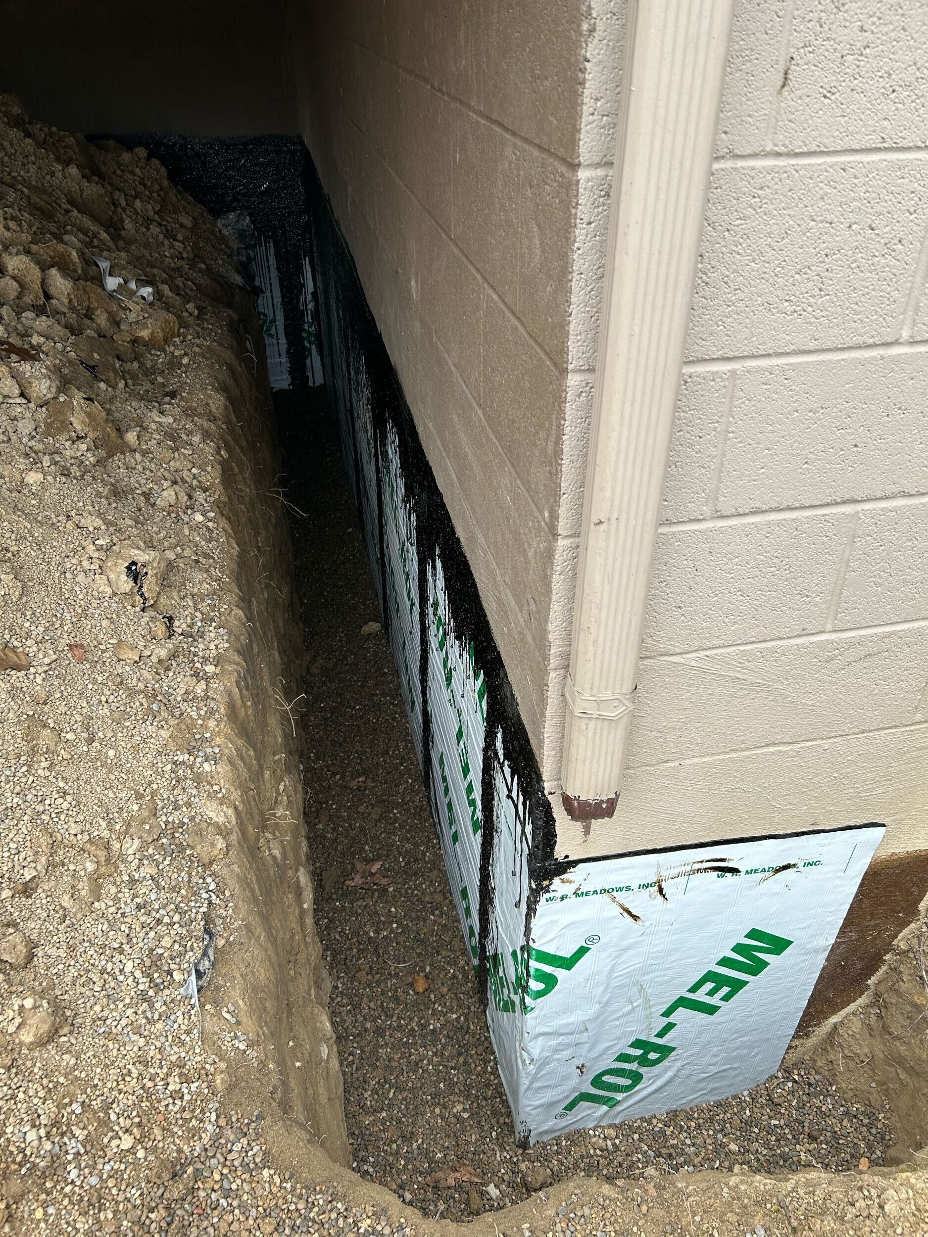 Corner of a building with exposed waterproofing and gravel ground beside the foundation