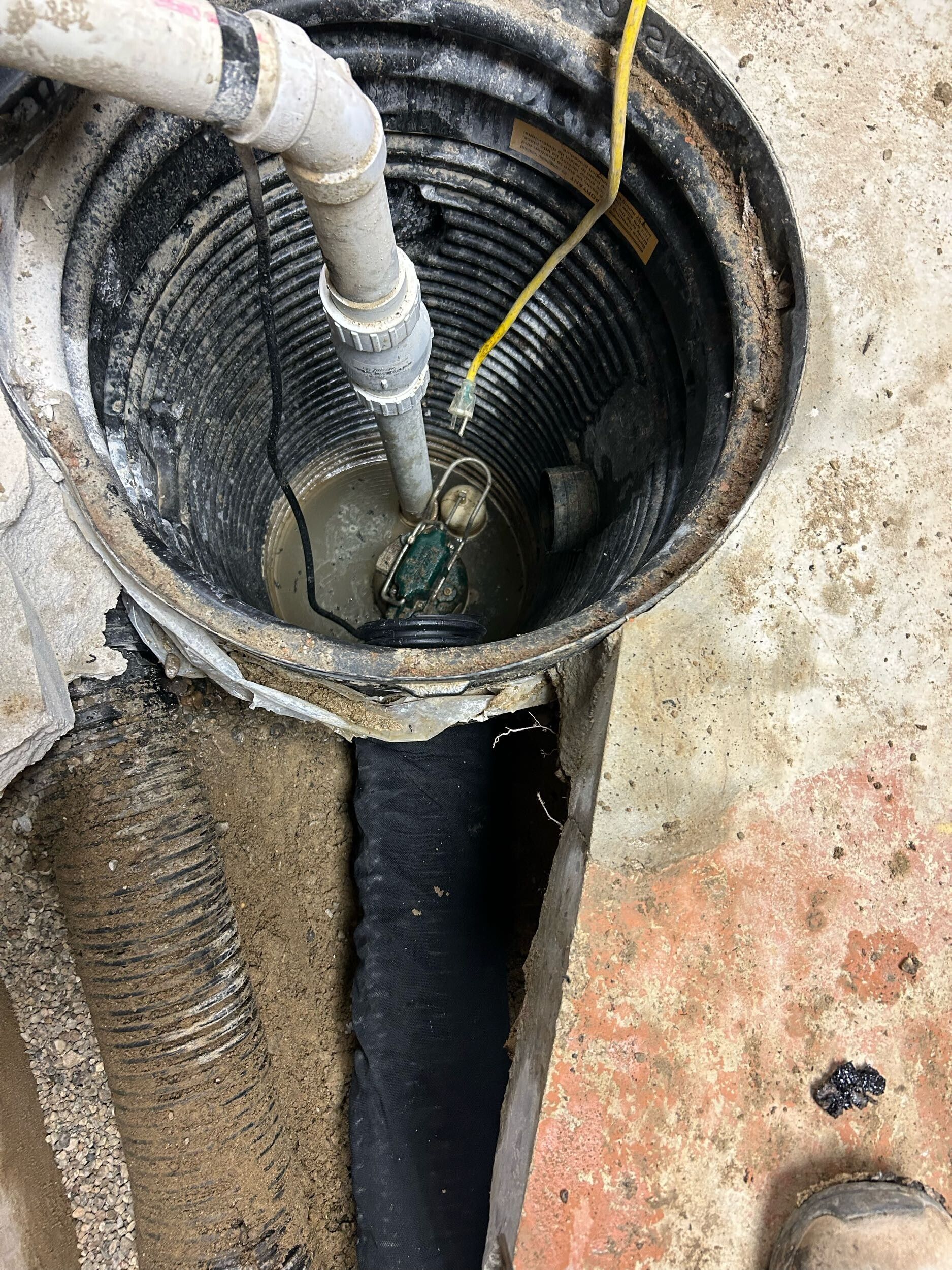 Open manhole with pipe and cable inside, showing a dark utility chamber surrounded by rough concrete.
