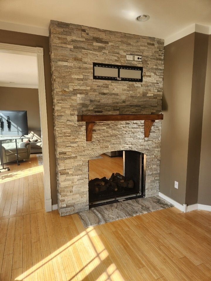 Living room fireplace with stone surround, wood mantel, and hardwood floor in sunlight