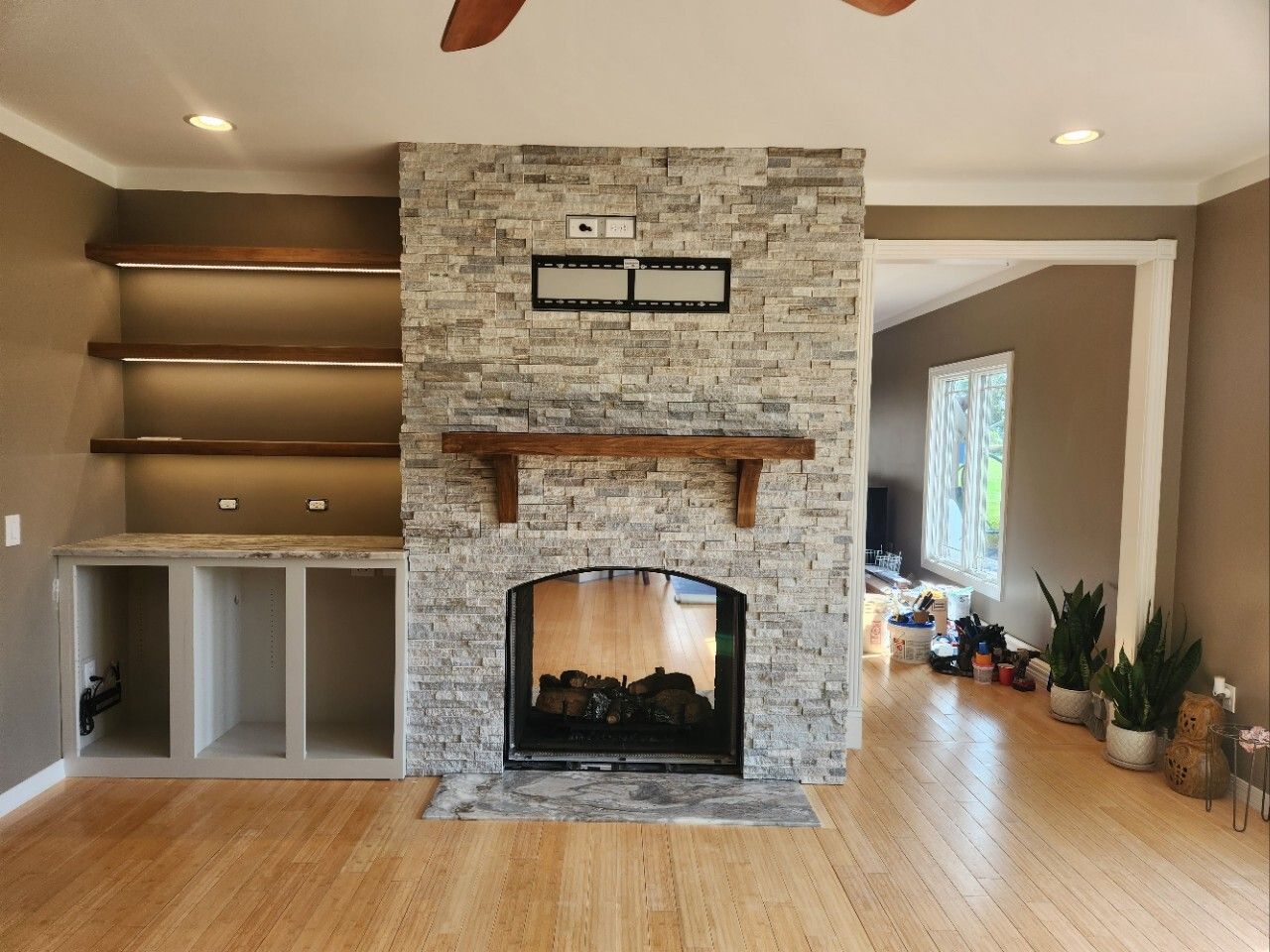 Living room with stone fireplace, built-in shelves, hardwood floors, and a doorway to the right