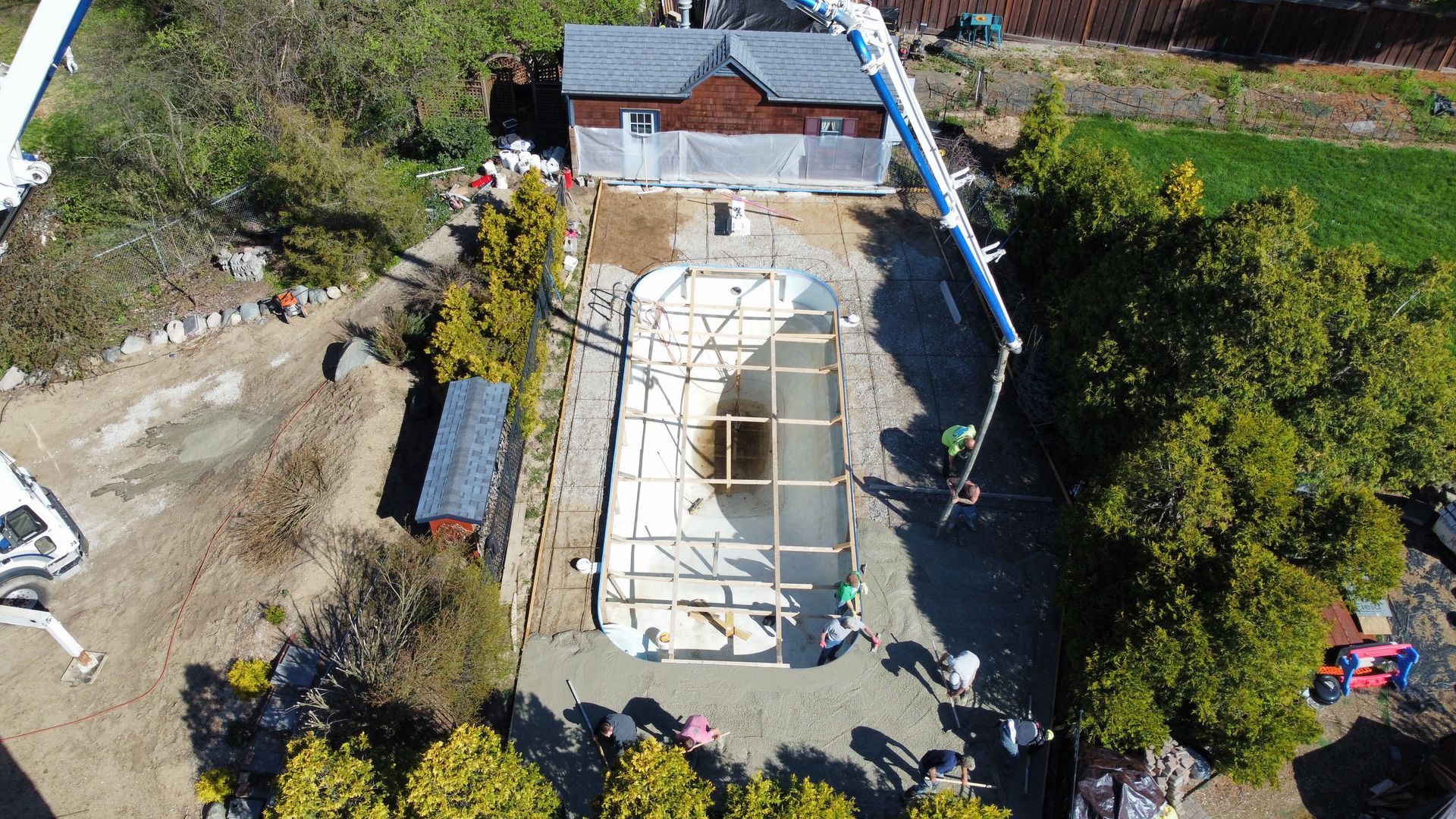 Aerial view of a construction site with a concrete structure, workers, and surrounding trees and dirt paths