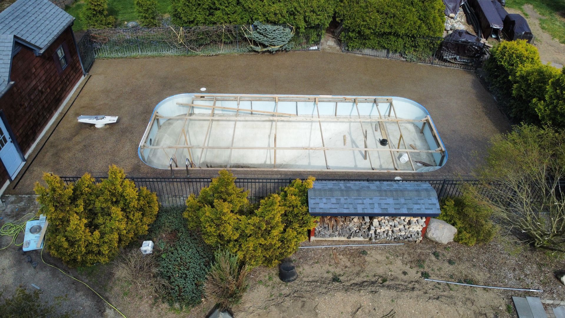 Aerial view of a covered swimming pool beside a house, with hedges and a paved yard.