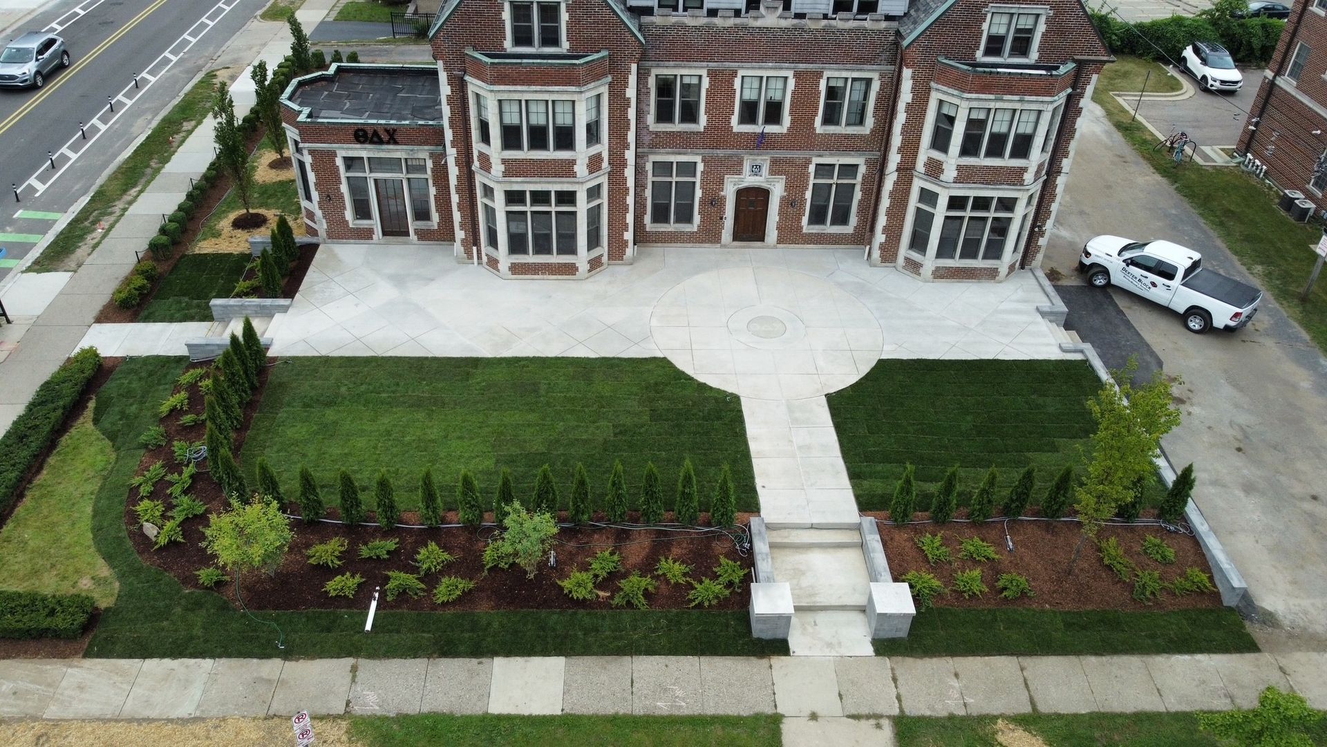 Aerial view of a brick building with a landscaped front lawn, walkway, and parked cars nearby