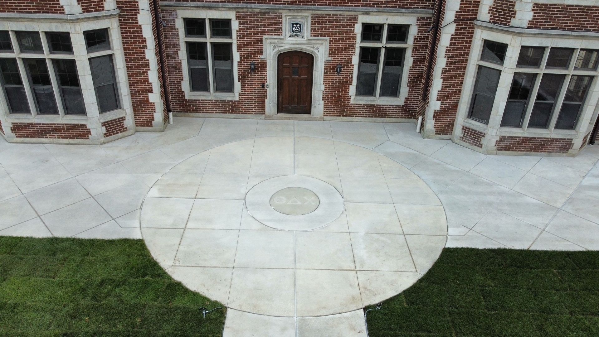 Brick building entrance with circular stone patio and surrounding grass, viewed from above