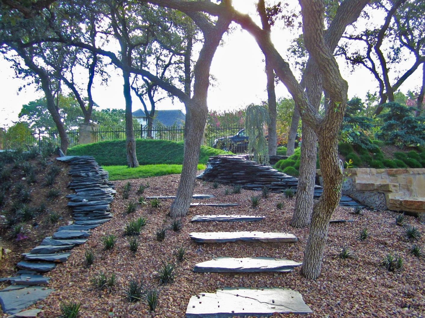 A stone pathway with flat steps leads through a wooded garden with mulch ground cover and stone retaining walls.