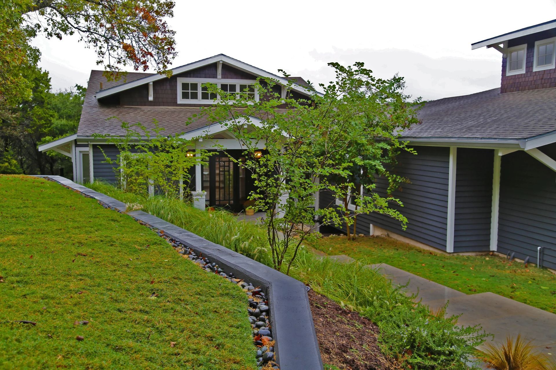 Dark gray building with sloped green lawn, a small tree, and a covered entrance.