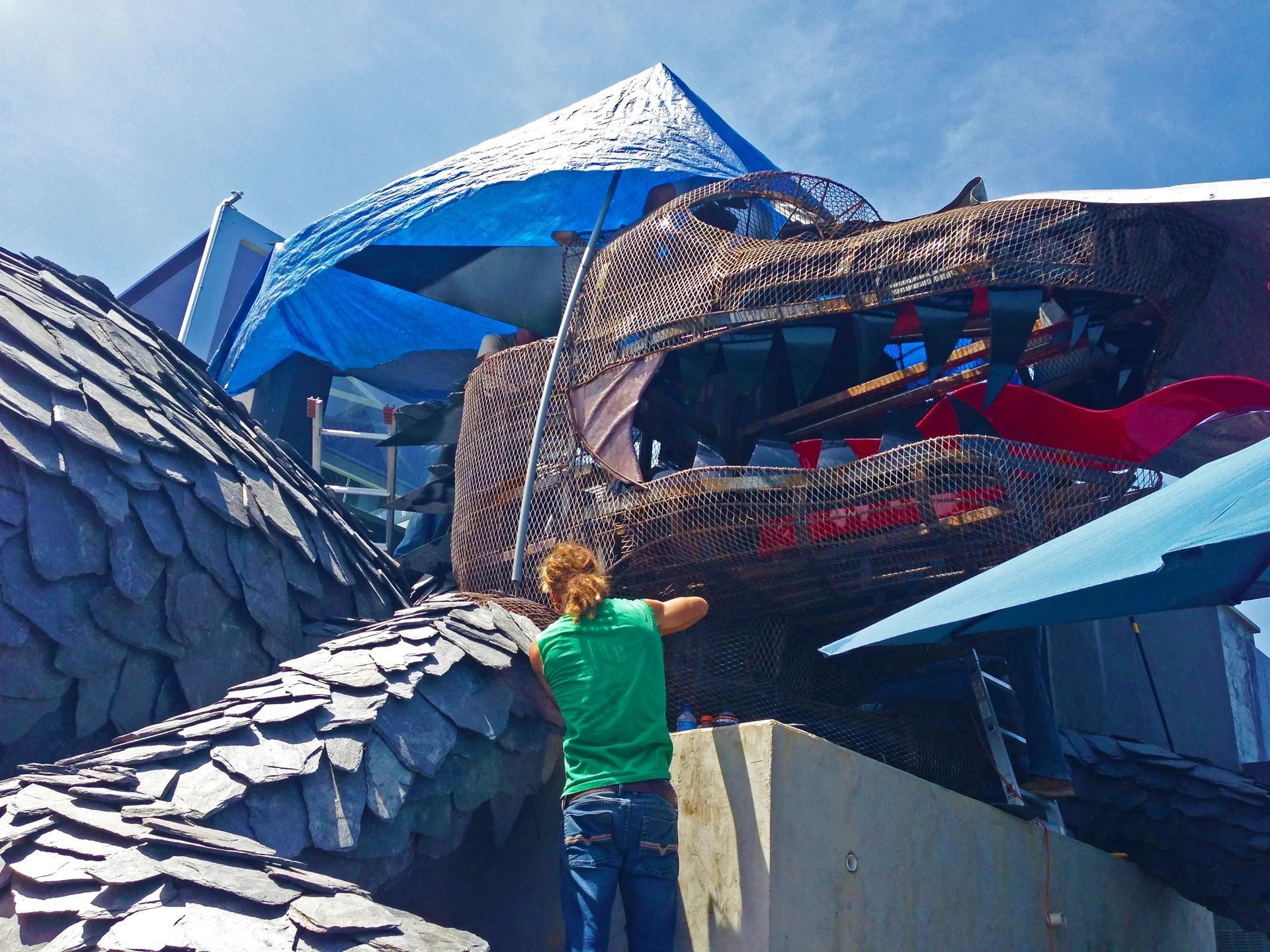 Person working on a large dragon sculpture with open mouth, part of a building facade.