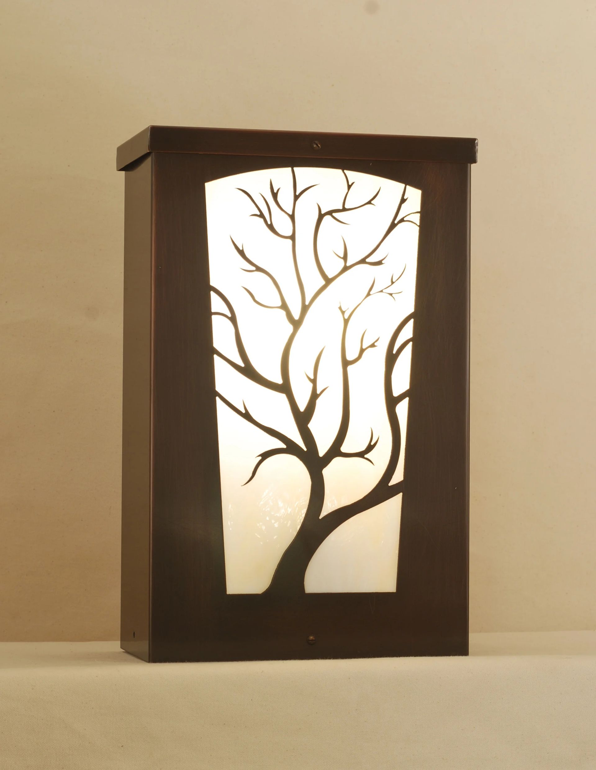 A dark brown rectangular wall sconce featuring a cutout design of a bare tree illuminated by a soft, warm white light.